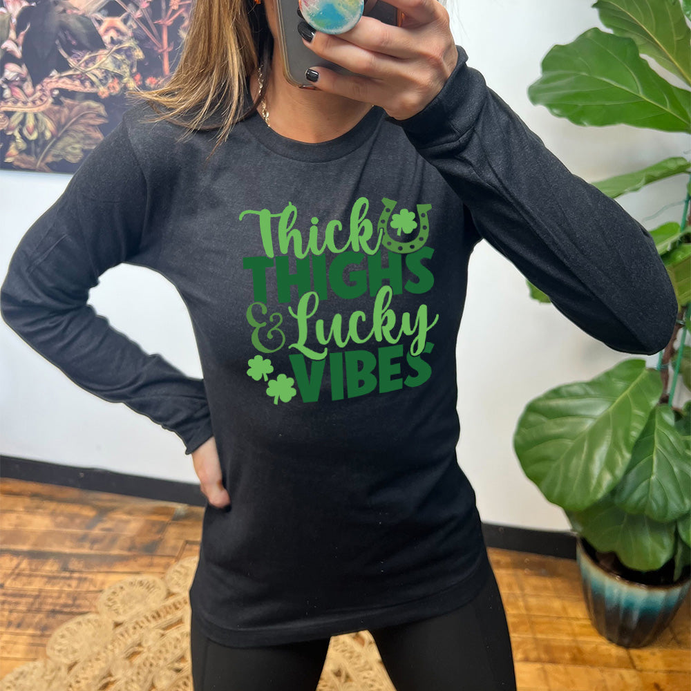 heather black long sleeve with the words "thick thighs & lucky vibes" on it, with graphics of a horseshoe and a few shamrocks