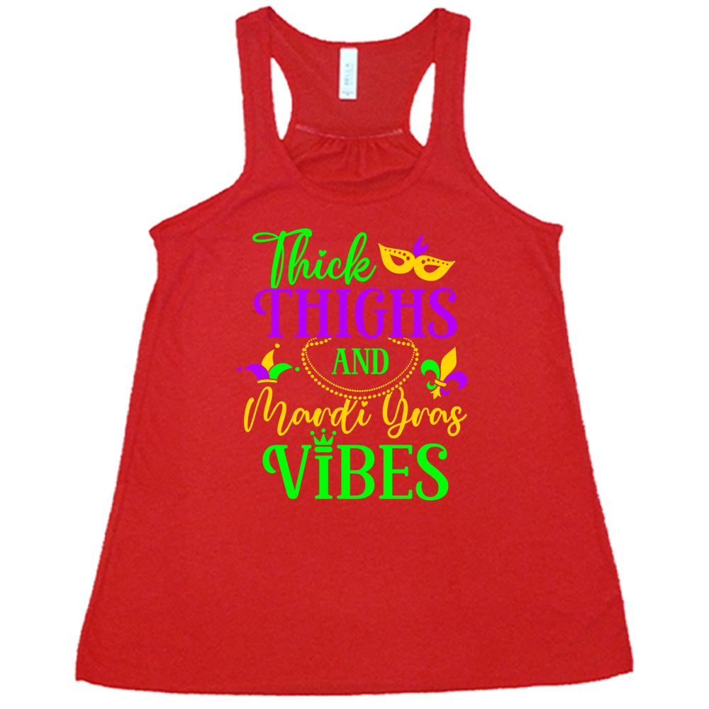 red flowy tank with the words "thick thighs and mardi gras vibes" on it in varying font, with small graphics of mardi gras beads, fleur de lis, a joker hat and a mask