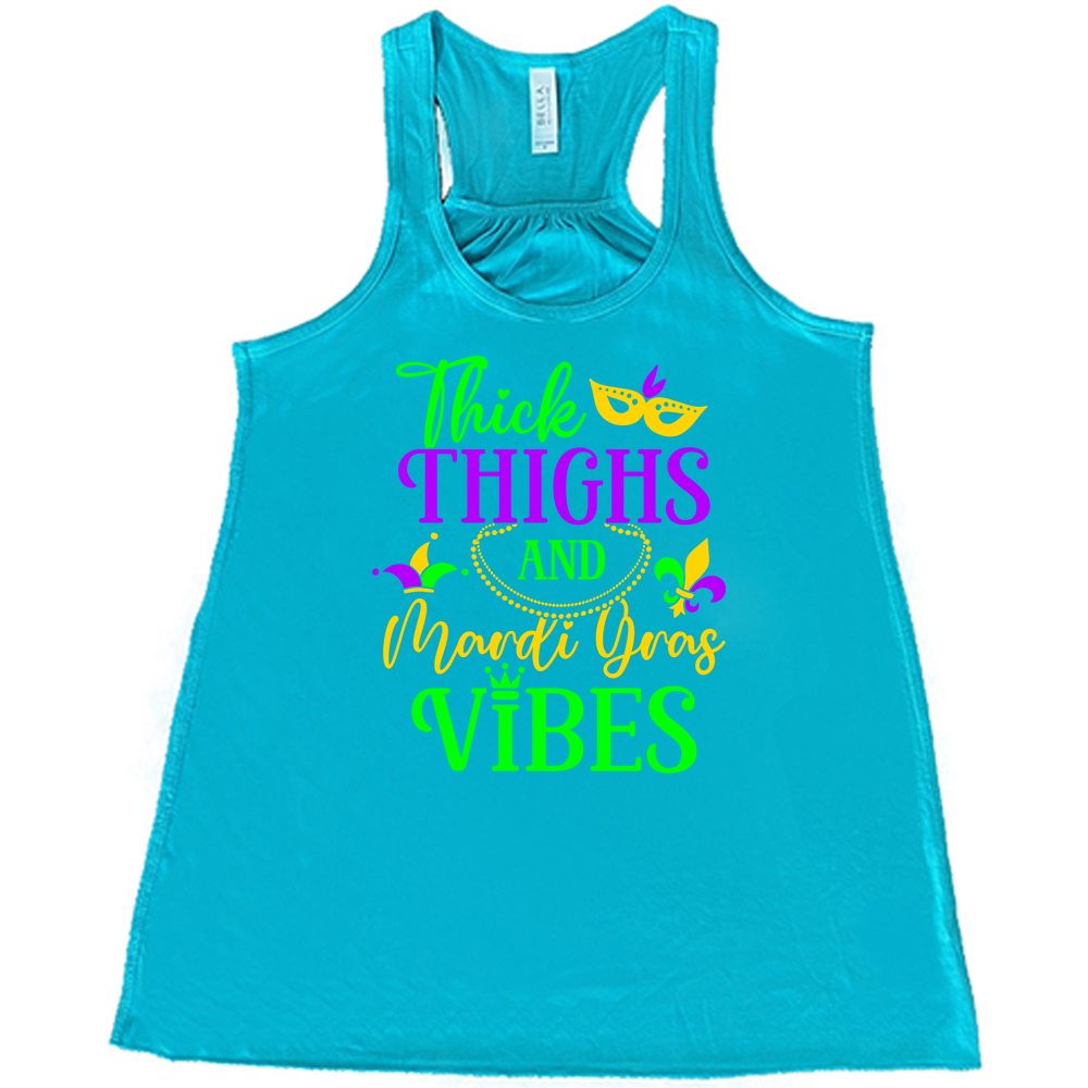 teal flowy tank with the words "thick thighs and mardi gras vibes" on it in varying font, with small graphics of mardi gras beads, fleur de lis, a joker hat and a mask