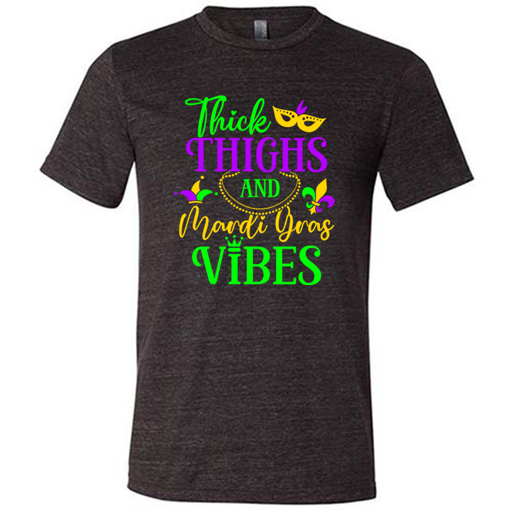 black unisex tee with the words "thick thighs and mardi gras vibes" on it in varying font, with small graphics of mardi gras beads, fleur de lis, a joker hat and a mask