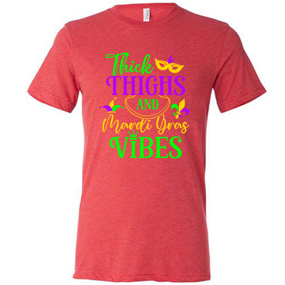 red unisex tee with the words "thick thighs and mardi gras vibes" on it in varying font, with small graphics of mardi gras beads, fleur de lis, a joker hat and a mask