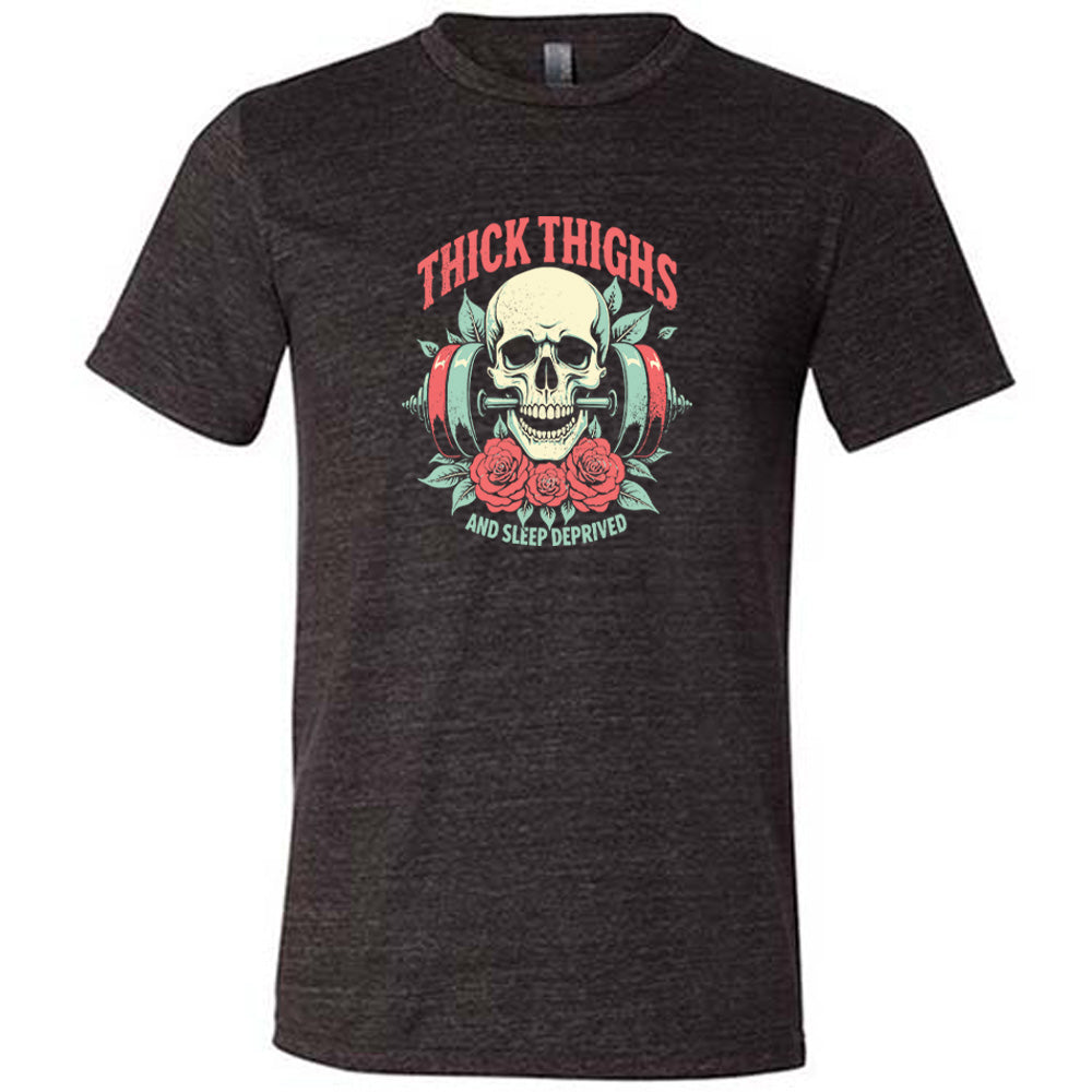 Black colored shirt with a skull, flowers, and barbell graphic on it that says "Thick Thighs And Sleep Deprived" 