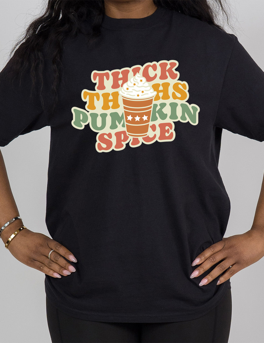 black modern tee with the words "thick thighs pumpkin spice" on it, with the graphic of a pumpkin spice latte, topped with whipped cream, in front of the words