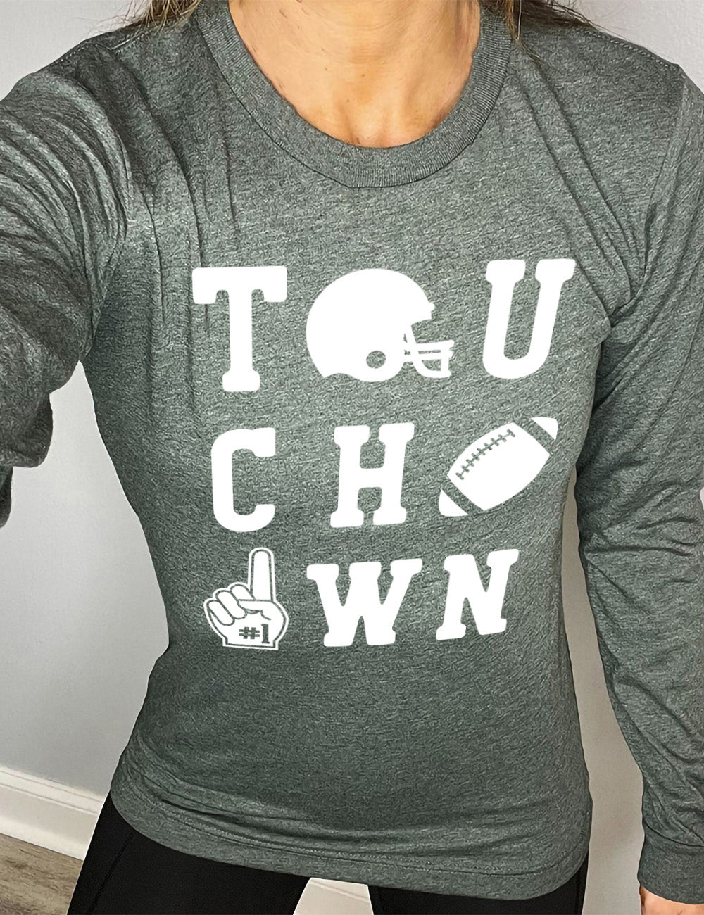 heather forest long sleeve tee with the word "touchdown" spelled out over three rows, and with the first "o" being a football helmet, the "d" being a football, and the last "o" being a foam finger with #1 on it