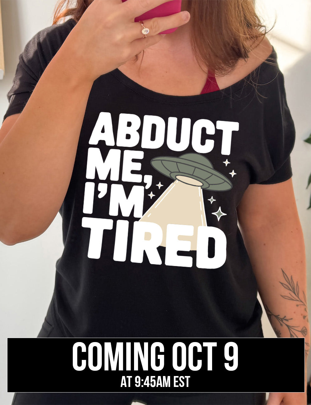black slouchy tee with the words "abduct me, I'm tired" on it, with a graphic of an alien spaceship, with a beam extended, and a few little stars, coming October 9th
