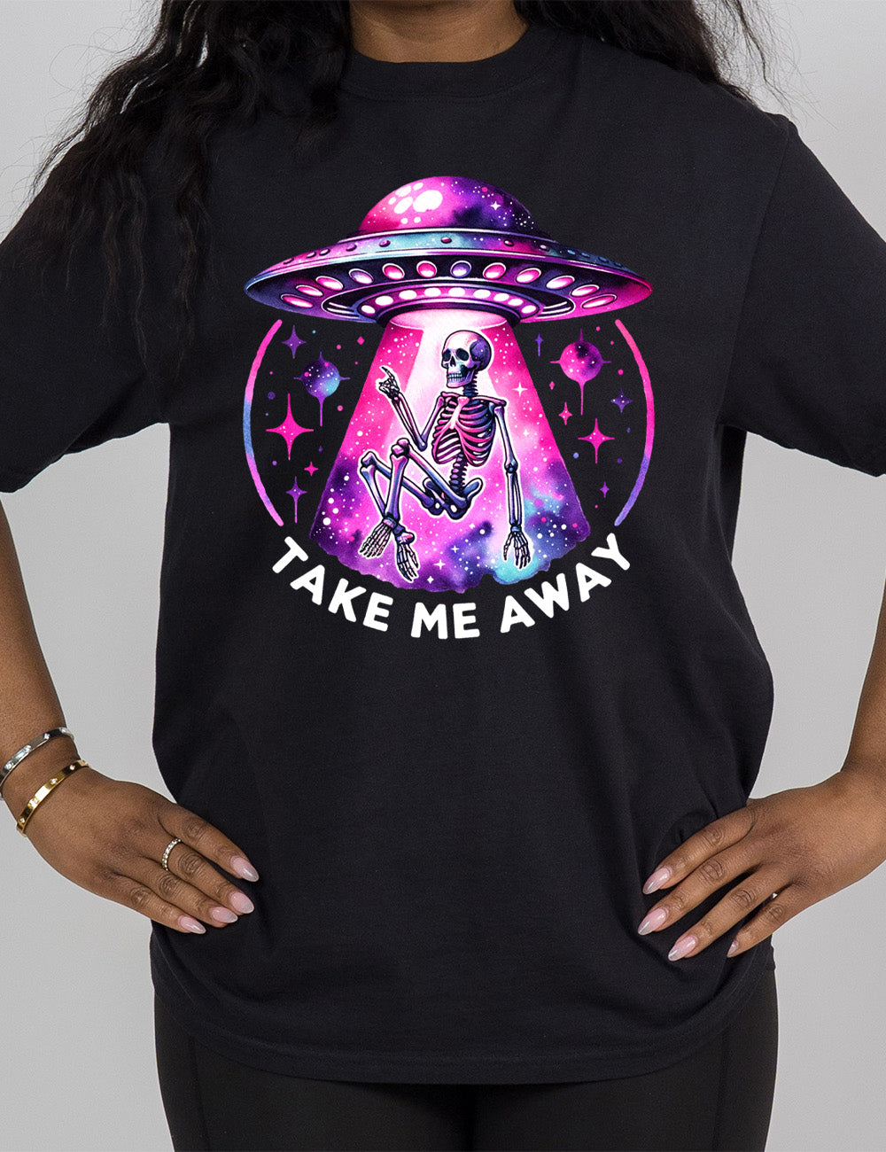 black modern tee with the colorful and detailed graphic of an alien spaceship, above little planets and stars, beaming up a skeleton, and the words underneath saying "take me away"
