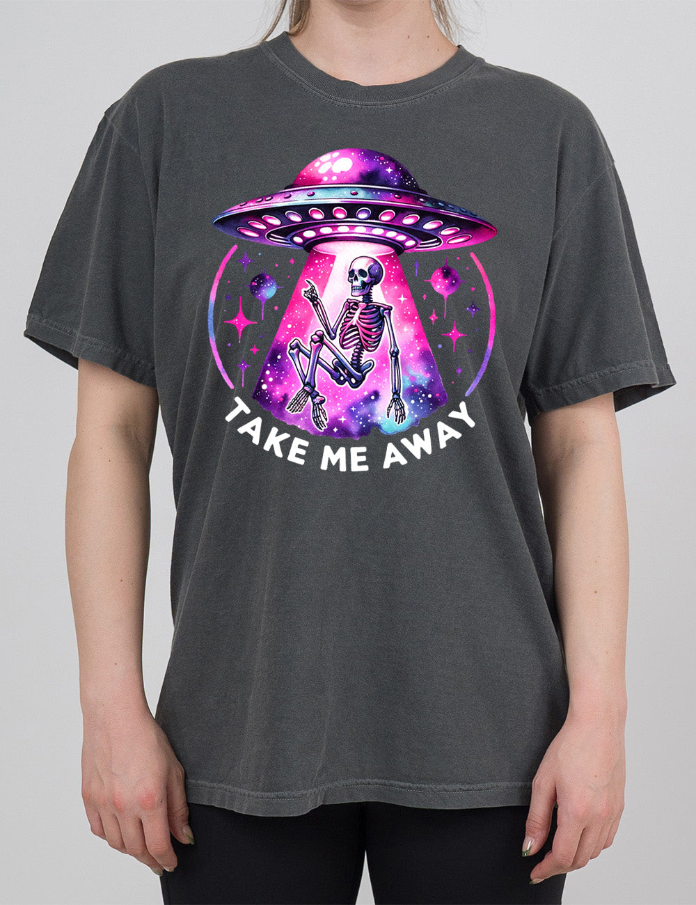 pepper modern tee with the colorful and detailed graphic of an alien spaceship, above little planets and stars, beaming up a skeleton, and the words underneath saying "take me away"