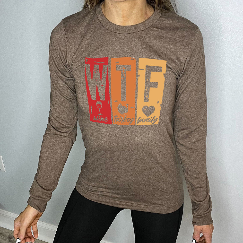 heather brown long sleeve shirt with a graphic on it that says "WTF" and under the "W" there's a graphic of a wine glass and the word "wine"; under "T" there's a graphic of a turkey and the word "turkey"; under F there's a graphic of a heart and the word "family"