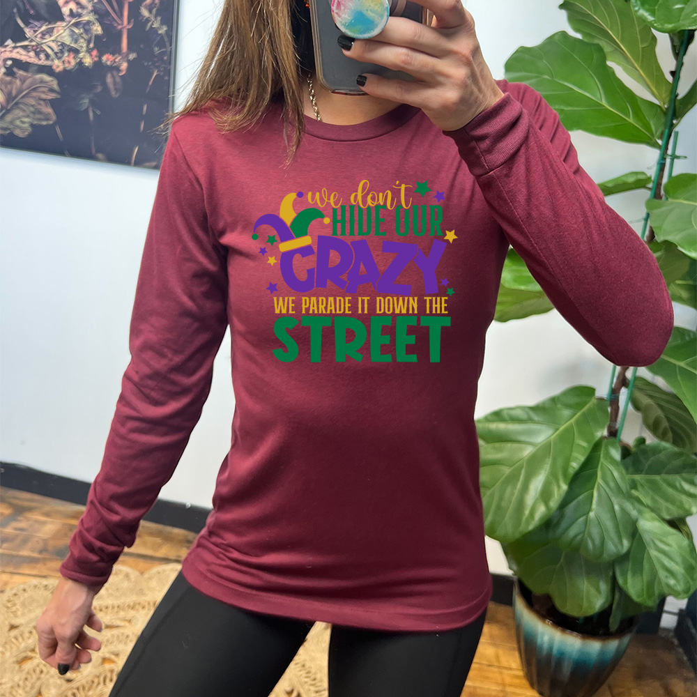 heather cardinal long sleeve tee with the words "we don't hide our crazy we parade it down the street" on it with a joker hat on the letter "c" and a few little stars scattered around