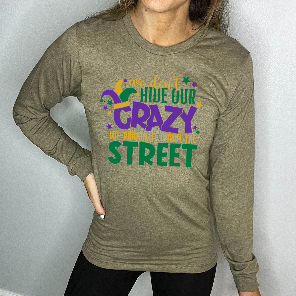 heather olive long sleeve tee with the words "we don't hide our crazy we parade it down the street" on it with a joker hat on the letter "c" and a few little stars scattered around