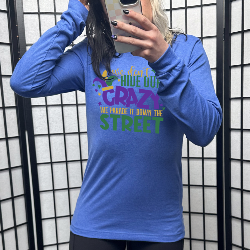 heather true royal long sleeve tee with the words "we don't hide our crazy we parade it down the street" on it with a joker hat on the letter "c" and a few little stars scattered around
