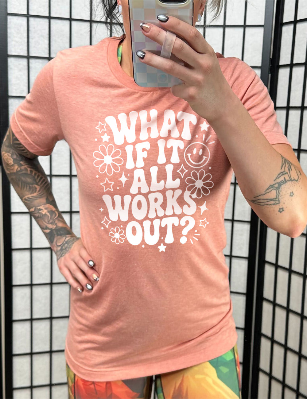 sunset unisex tee with wording saying "what if it all works out?" with graphics of flowers and stars as well as a smiley face