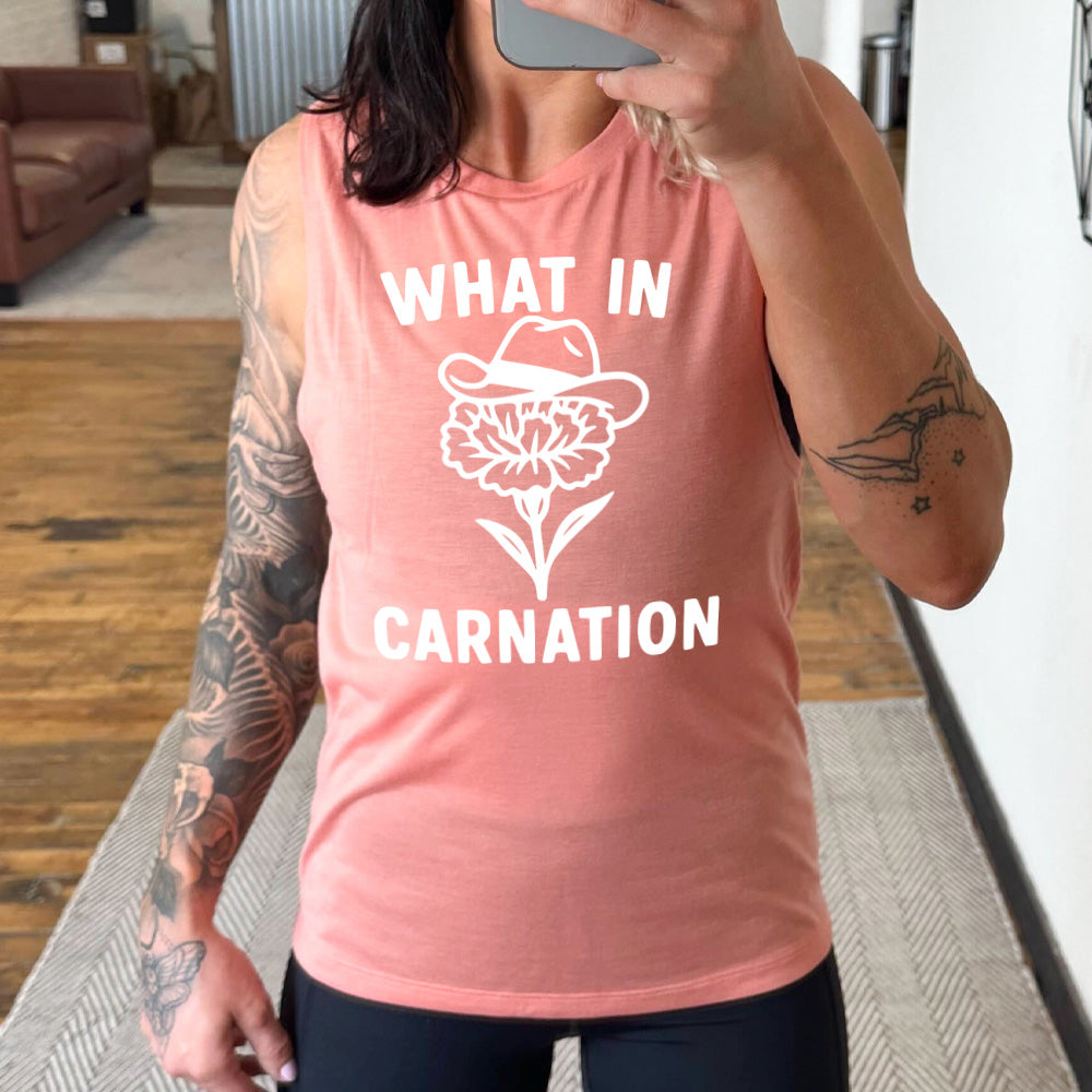 peach muscle tank with the words "What in carnation" on it, around the graphic of a carnation, wearing a cowboy hat