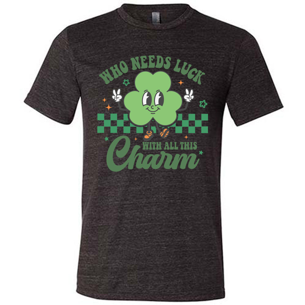 black unisex tee with the words "who needs luck with all this charm" on it, with the graphic of a cheerful shamrock (with eyes, nose and smiling mouth) giving two peace signs with its hands, in front of a partial checkered background, with a few stars around