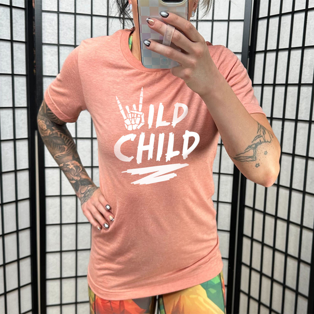 Model wearing sunset colored shirt with a skeleton hand signing rock on graphic on it that says "Wild Child" 