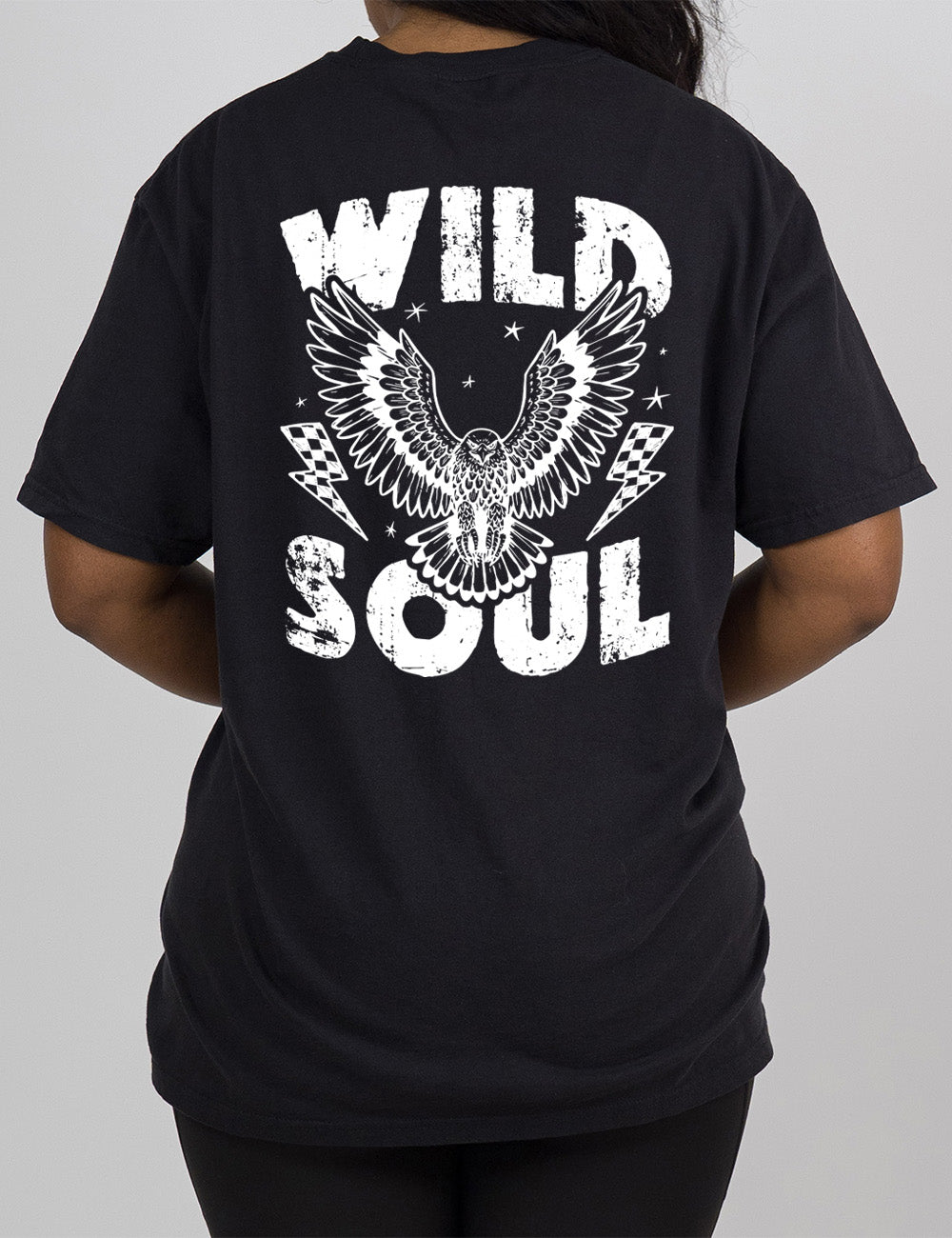 black modern tee with print placement on the back, with the words "wild soul" on it, with a large eagle graphic, with wings in flight, in the middle of the words, with a checkered lightning bolt on either side of it, with a few stars scattered around it