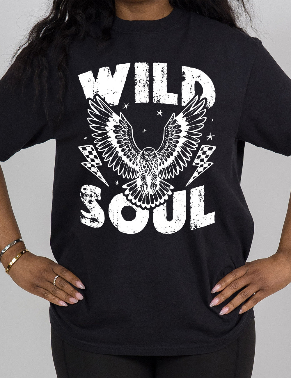 black modern tee with print placement on the front, with the words "wild soul" on it, with a large eagle graphic, with wings in flight, in the middle of the words, with a checkered lightning bolt on either side of it, with a few stars scattered around it