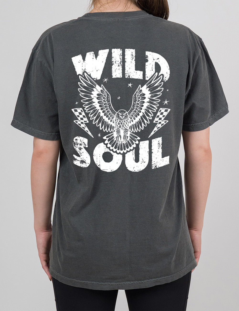 pepper modern tee with print placement on the back, with the words "wild soul" on it, with a large eagle graphic, with wings in flight, in the middle of the words, with a checkered lightning bolt on either side of it, with a few stars scattered around it