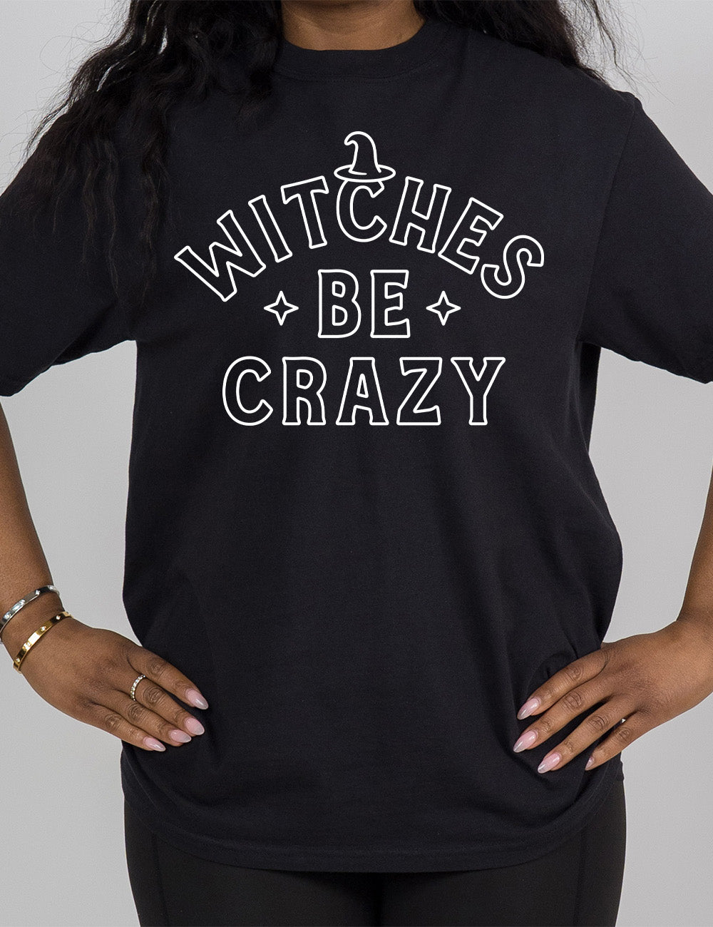 black modern tee with the words in outline font saying "witches be crazy" with a witch hat on top of the "c" in "witches" and a star on either side of the word "be"