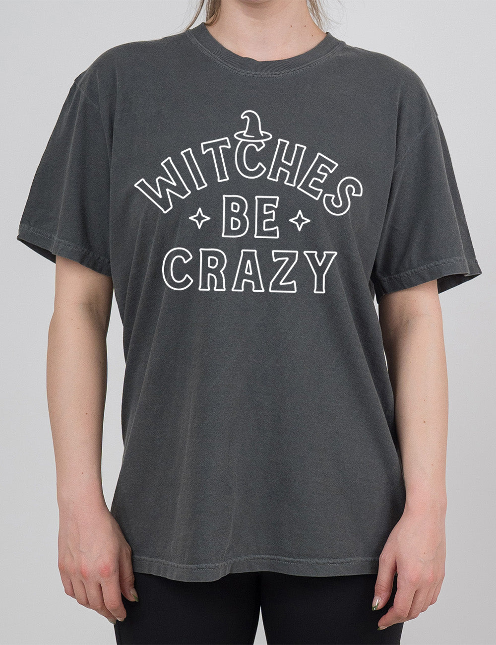 pepper modern tee with the words in outline font saying "witches be crazy" with a witch hat on top of the "c" in "witches" and a star on either side of the word "be"
