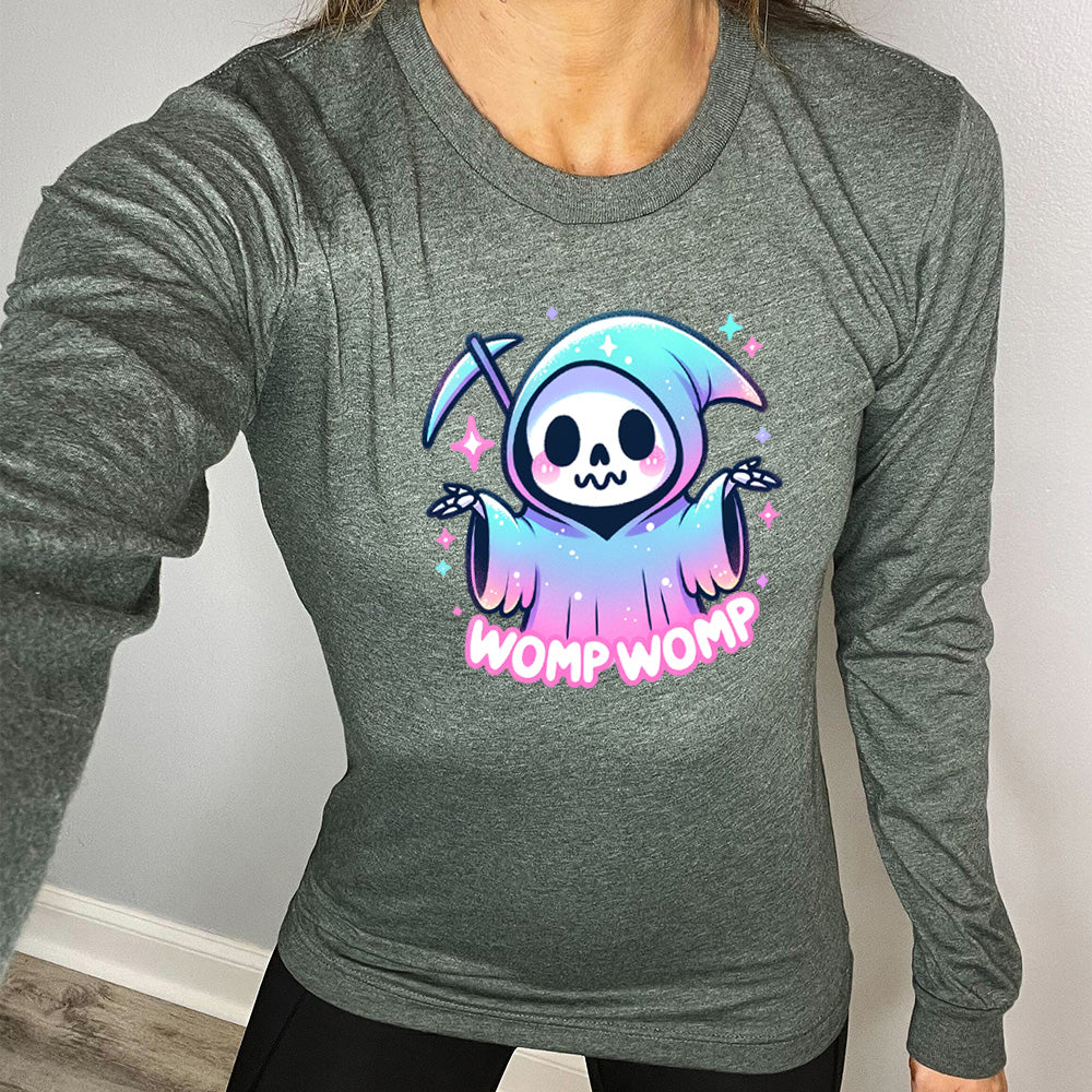 heather forest long sleeve shirt with the text "Womp Womp" on it, with the cartoon graphic of a sparkly-robed grim reaper, skeletal hands raised in question, surrounded by sparkly little stars