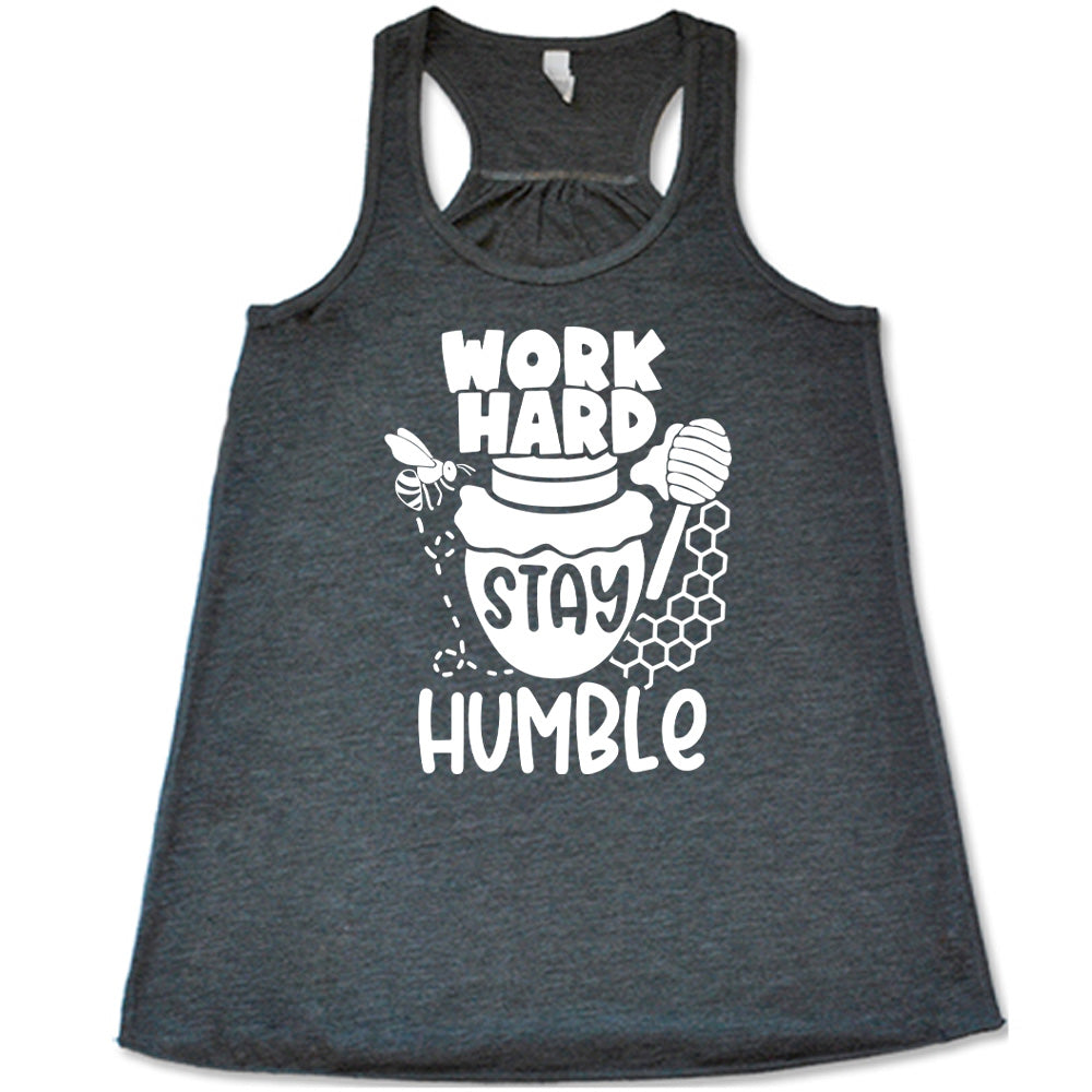 grey flowy racerback tank with the words "work hard stay humble" on it, with the word "stay" on the graphic of a honeypot, and a bee flying around the pot's left, and some honeycomb and a honey spoon on its right