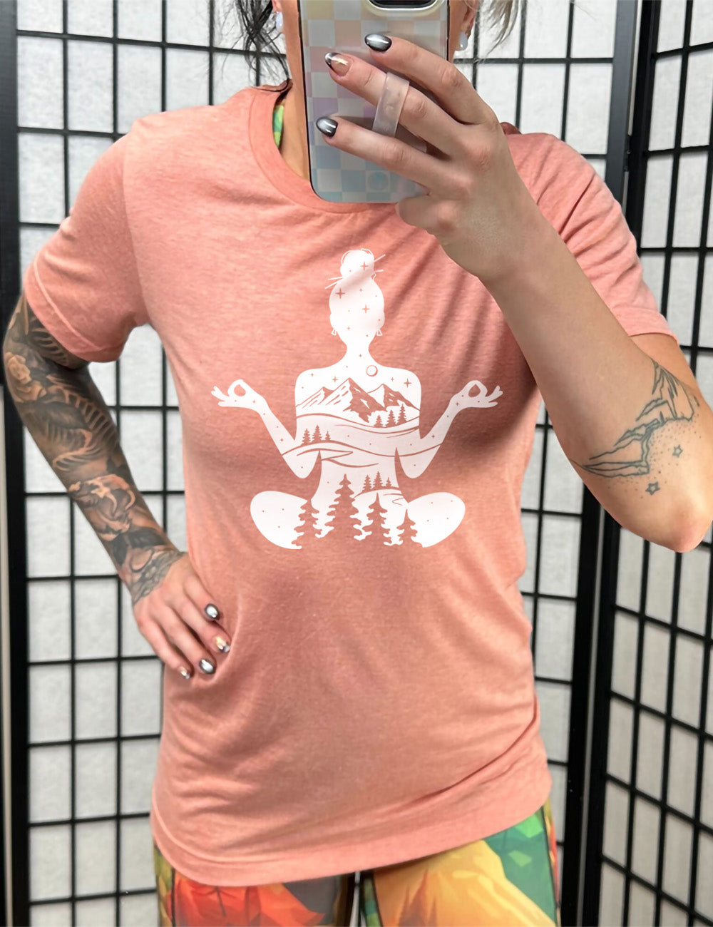 sunset unisex tee with the graphic of a woman's silhouette, doing a yoga pose, with her body made up of a forest, field, mountain and starry landscape