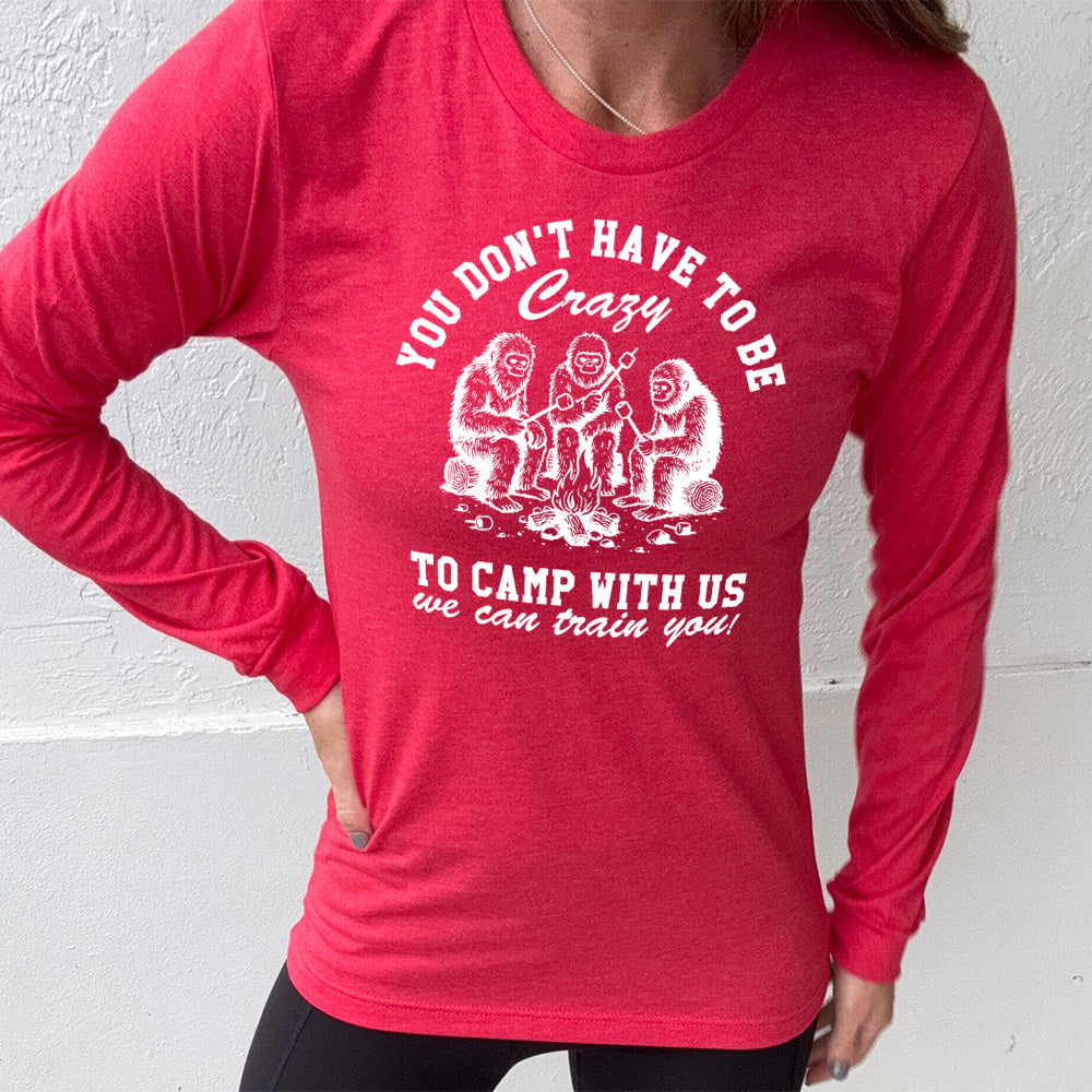 heather red long sleeve with the words "you don't have to be crazy to camp with us we can train you!" on it with the graphic of three sasquatches   toasting marshmallows over a campfire