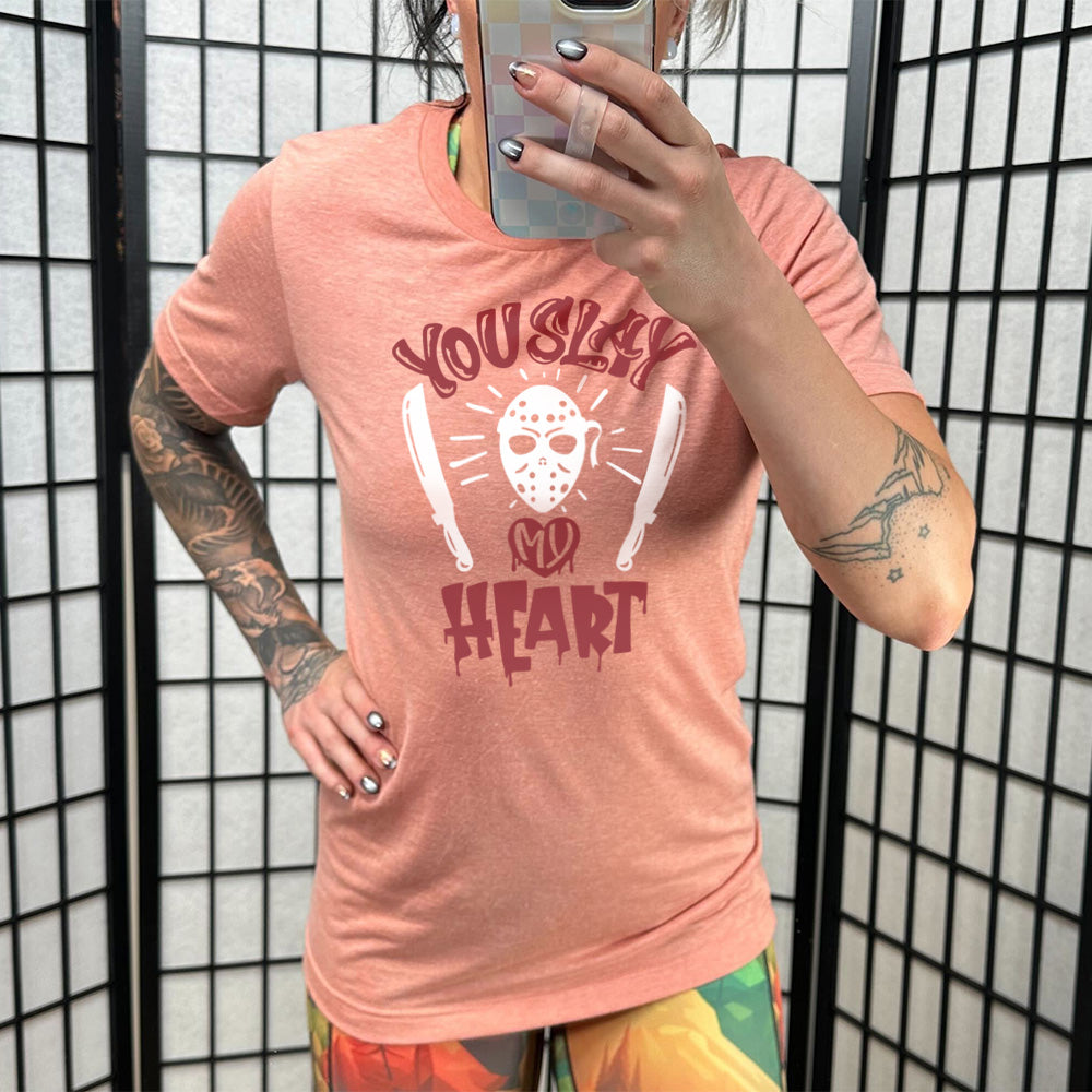 sunset unisex tee with the words "you slay my heart" on it in horror movie style writing, with "my' being in a dripping heart, and graphics of the Jason mask from Friday the 13th and two machetes 