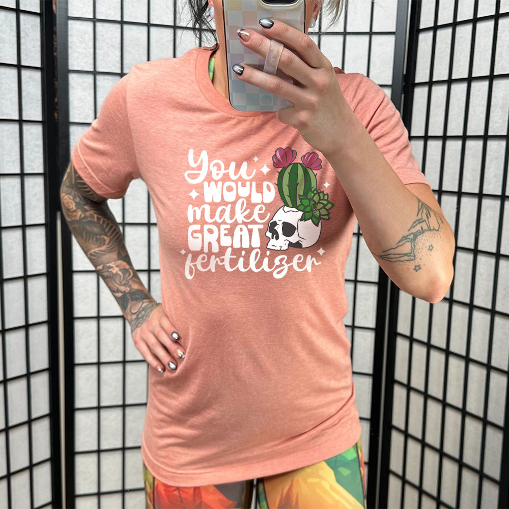 Model wearing sunset colored shirt with a cactus growing from a skull graphic on it that says "You Would Make Great Fertilizer" 