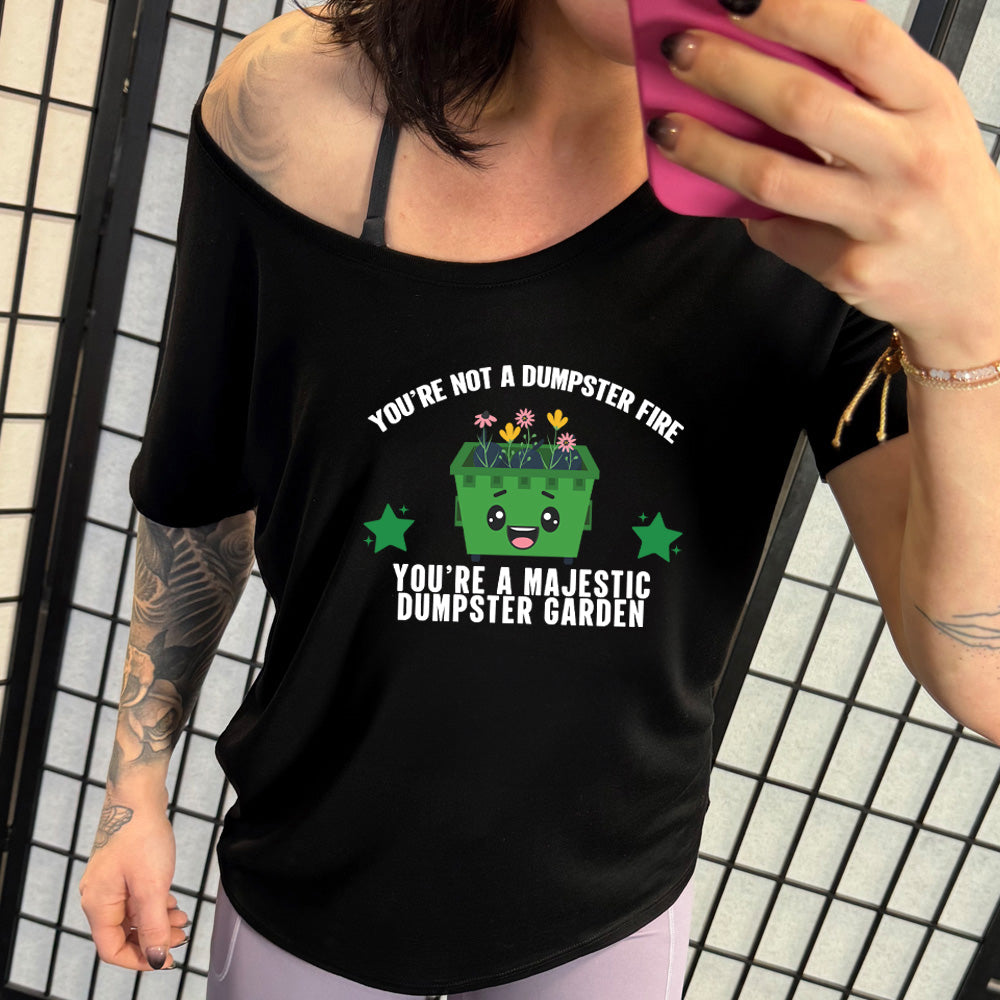 Black colored shirt with a dumpster and flowers graphic on it that says "You're Not A Dumpster Fire, You're A Majestic Dumpster Garden"