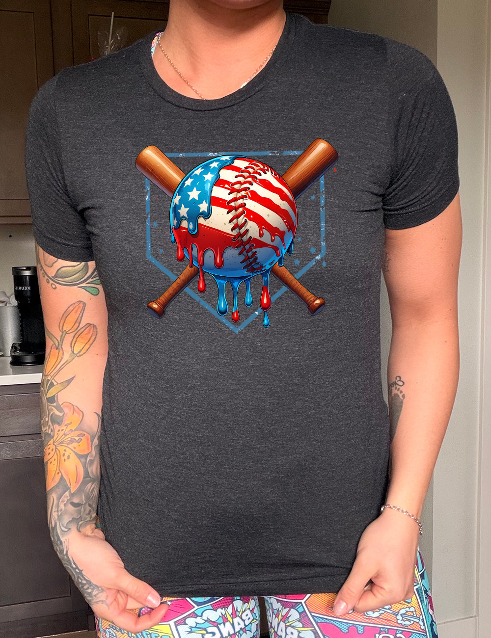 black unisex tee with the graphic of a baseball painted (and dripping) with the American flag, and two baseball bats crossed behind it, all in front of a starry baseball diamond