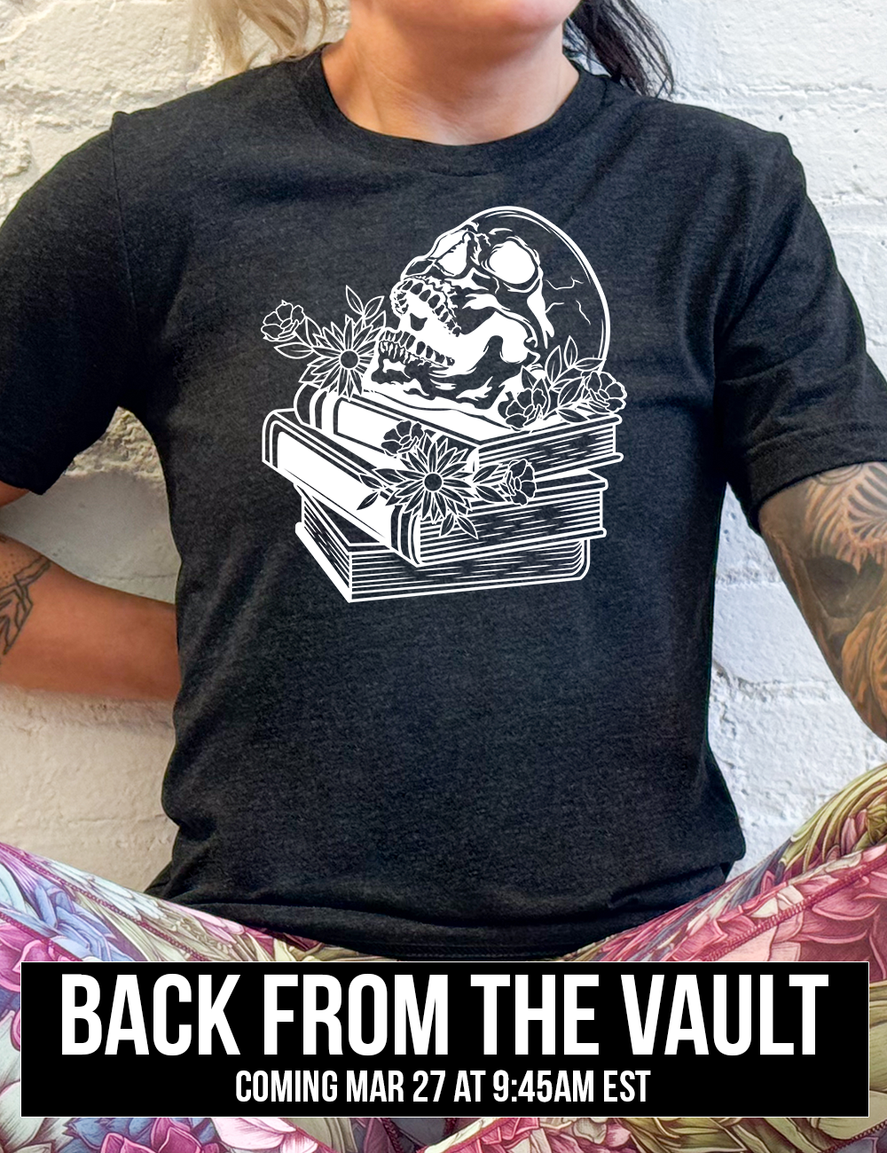 black unisex tee with the graphic of an open-mouthed skull atop a stack of books, with flowers, coming soon
