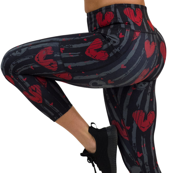 close up of red heart and gray skulls against a black and grey striped background leggings against a white background