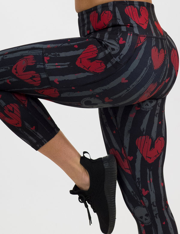 close up of red heart and gray skulls against a black and grey striped background leggings against a white background