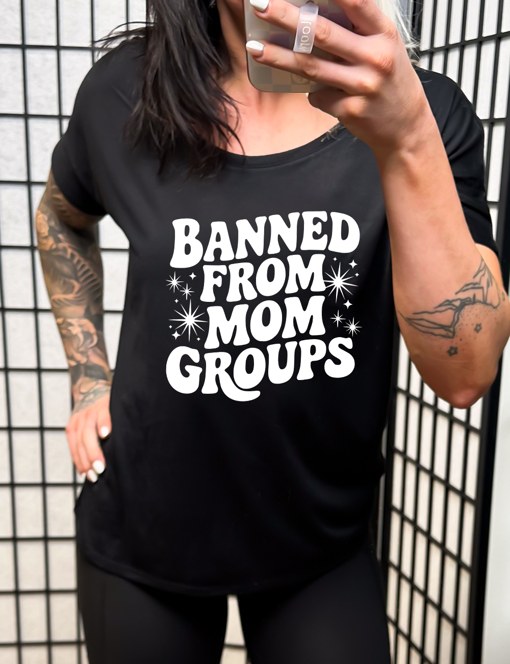 black slouchy tee with the words "banned from mom groups" on it, with stars on either side of the words "from mom"