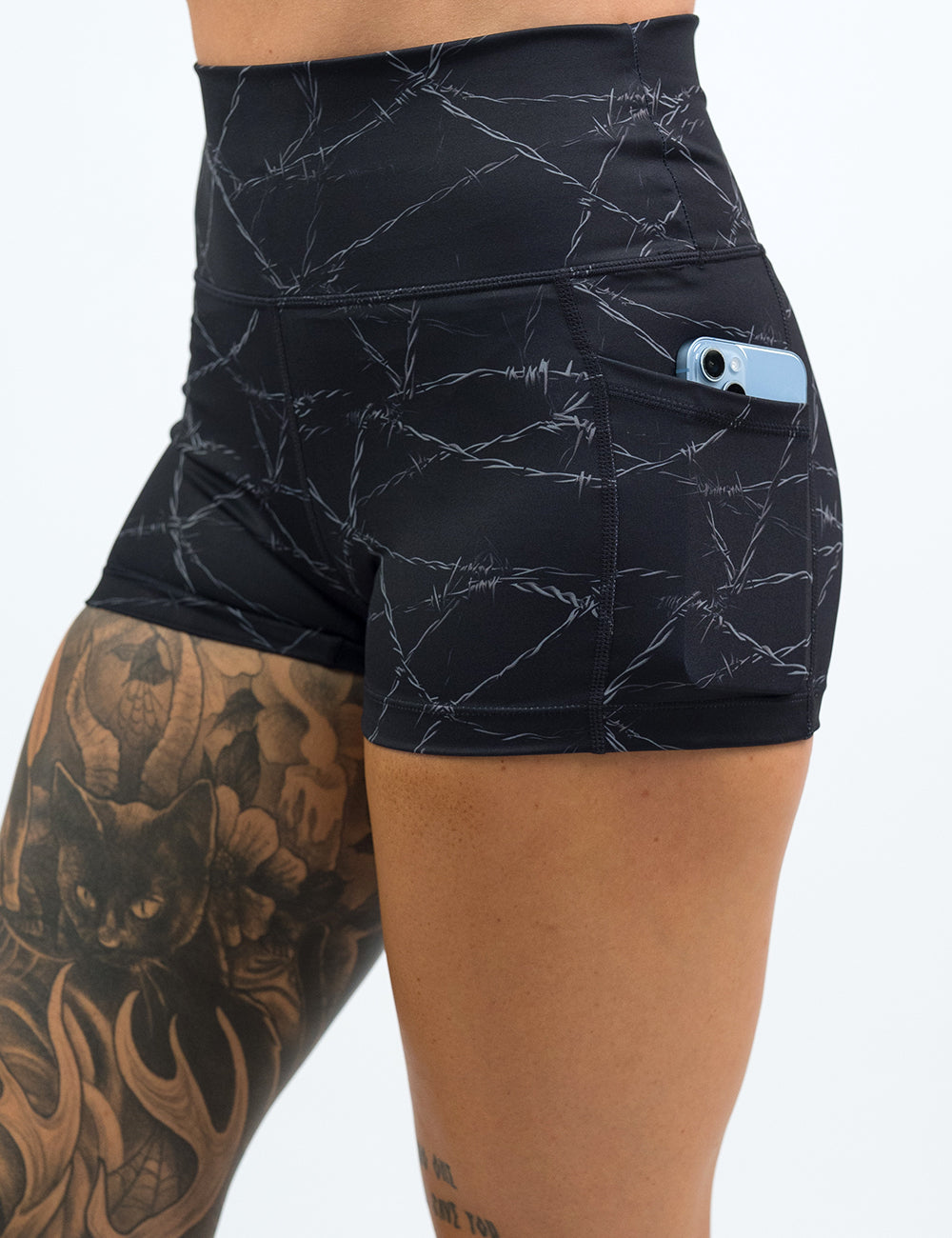 Close up of the 3.5 inch black shorts with a white barbed wire pattern on it holding a phone