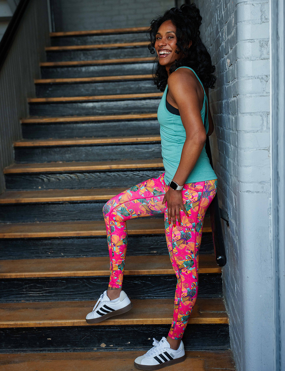 model wearing the full length red starfish with a yellow and blue shell background leggings in a stairwell