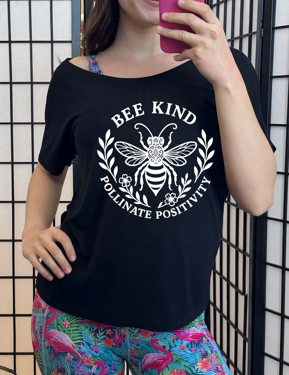 black slouchy tee with the words "bee kind pollinate positivity" on it, arranged in two arcs, forming a circled effect, with two branches and two flowered branches within the circle, and a large fancy bee in the center
