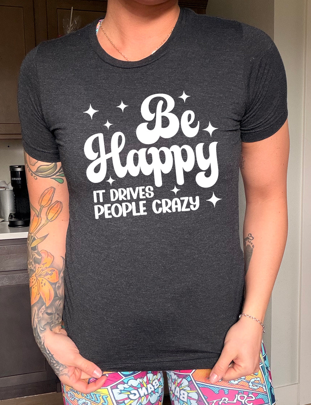 black unisex tee with the words "be happy it drives people crazy" on it, with a number of stars around