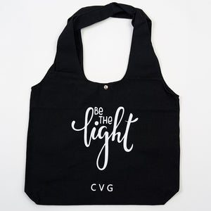 "be the light" saying on a black tote bag
