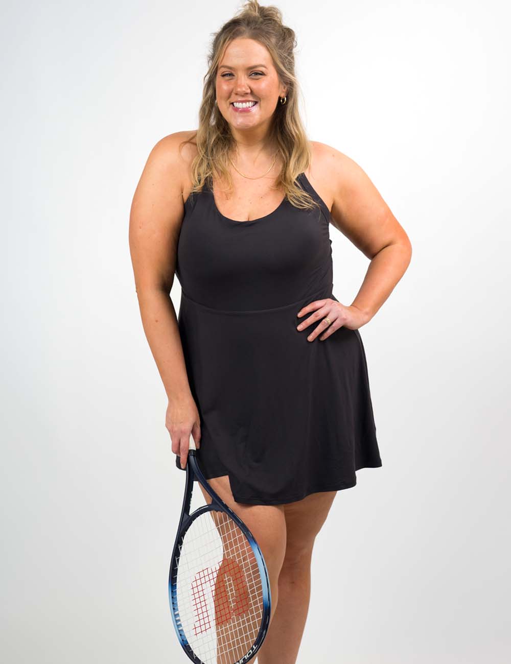 Woman in a black tennis dress holding a racket on a white background