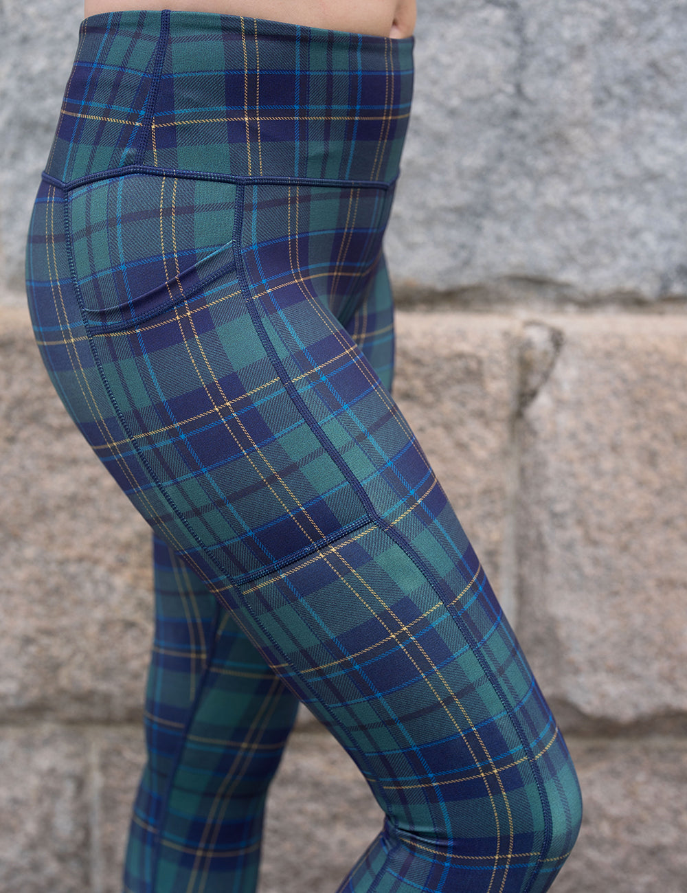 close up of the blue, green, and yellow plaid leggings against a stone wall