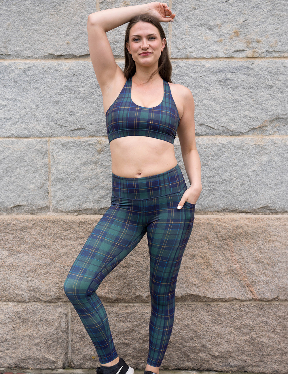 model wearing the blue, green, and yellow plaid full length leggings and bra in front of a stone wall