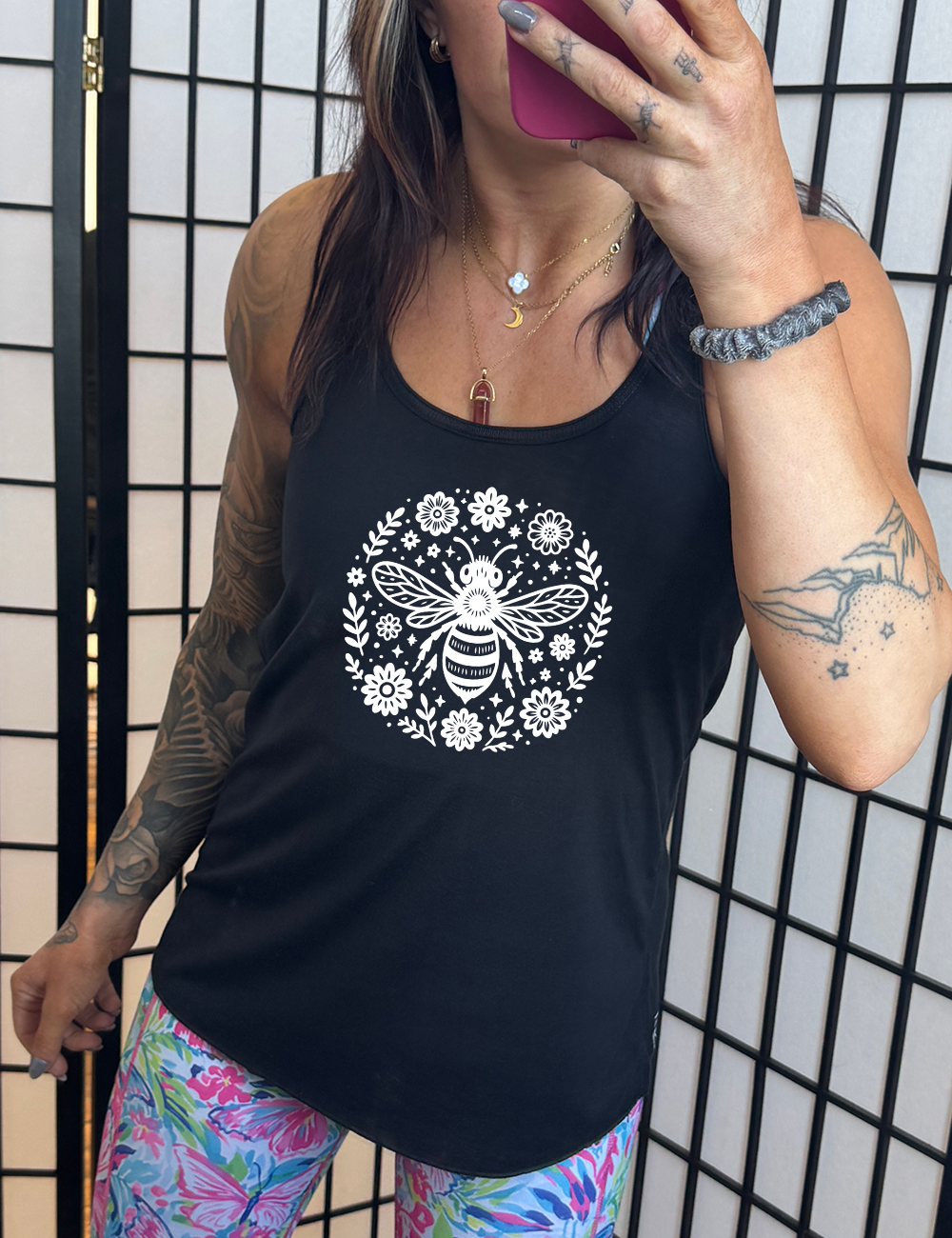 black flowy racerback tank with the graphic of a boho circled design filled with flowers of varied size, some branches, some stars, and in the center a fancy bee