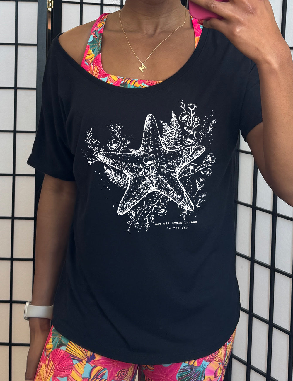 black slouchy tee with the graphic of a very detailed starfish among sea plants and flowers, with little bubbles, and the small words underneath it all that say "not all stars belong to the sky"