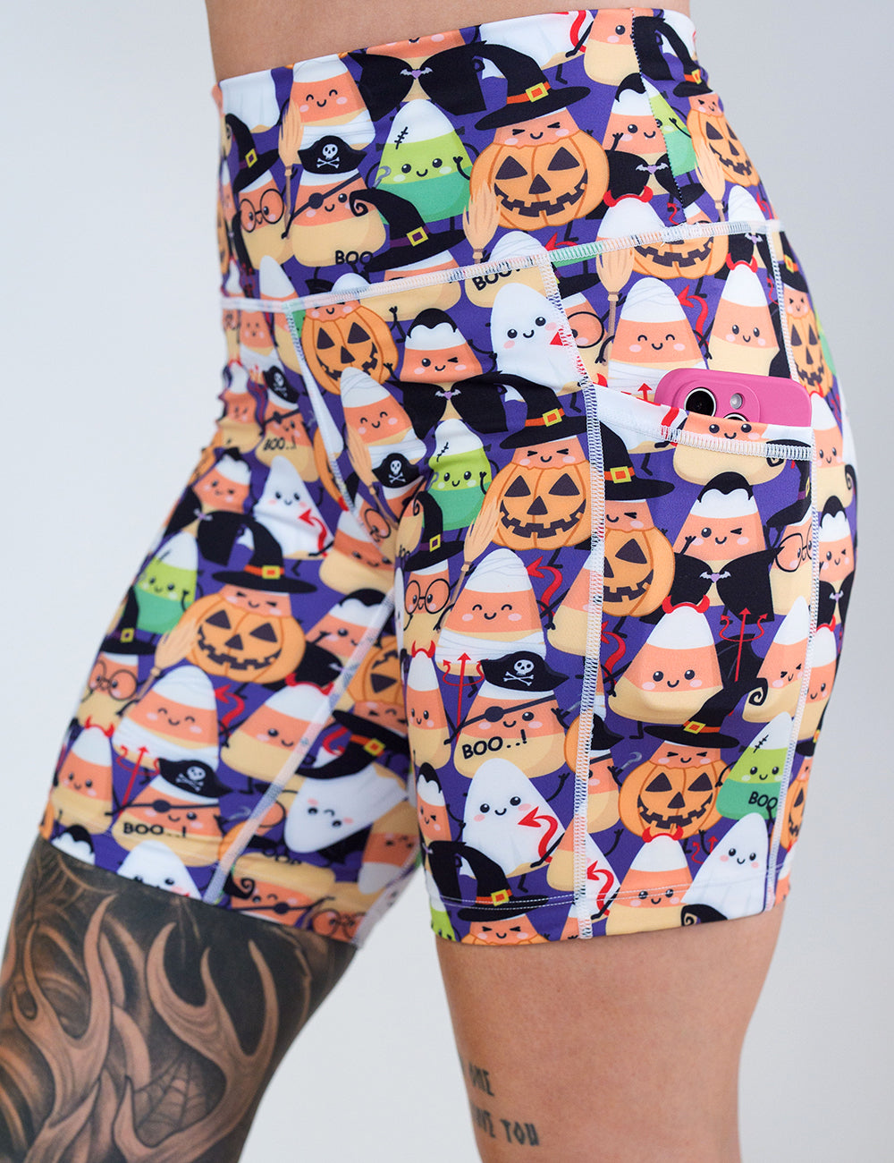 close up of the 5 inch halloween candy corn patterned shorts holding a phone in the pocket