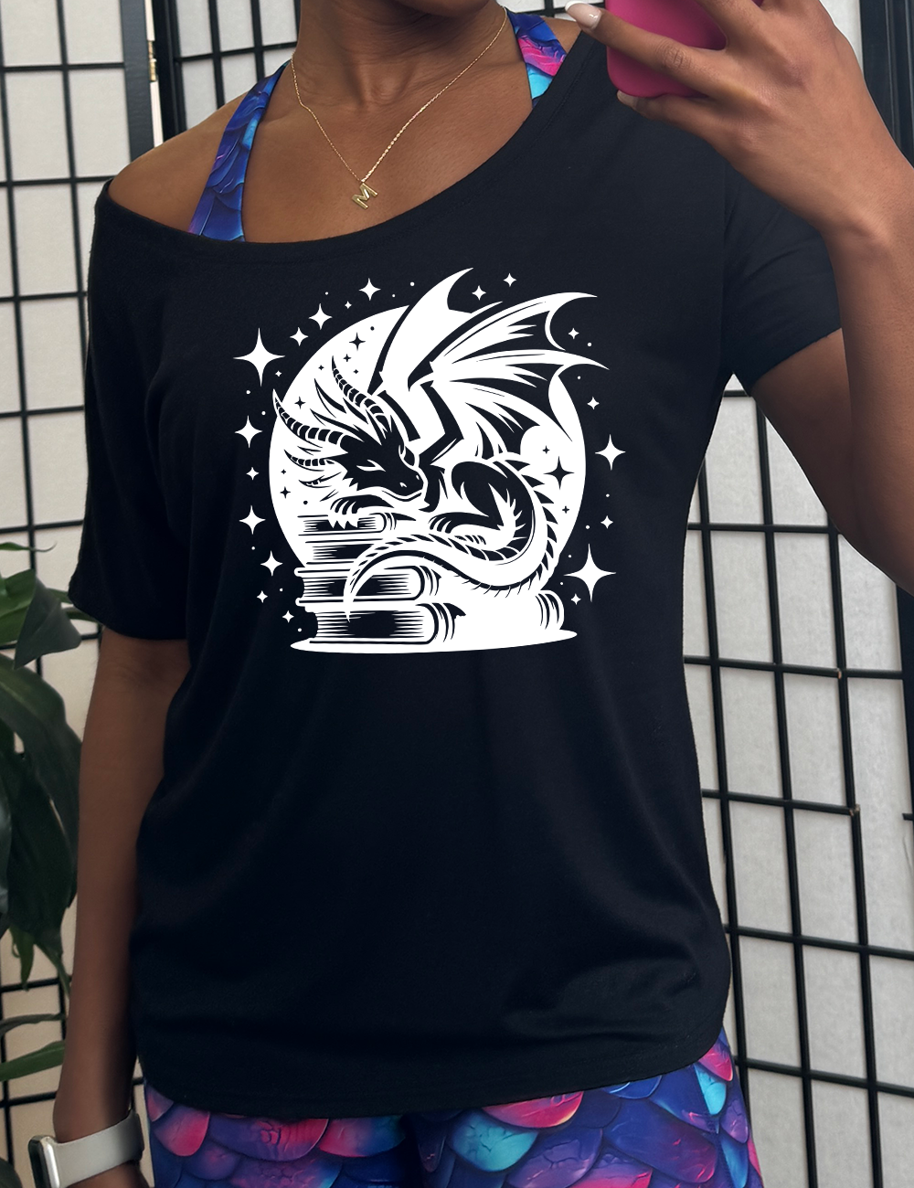 black slouchy tee with the graphic of a dragon resting on a stack of books, in front of a full moon, with many stars around