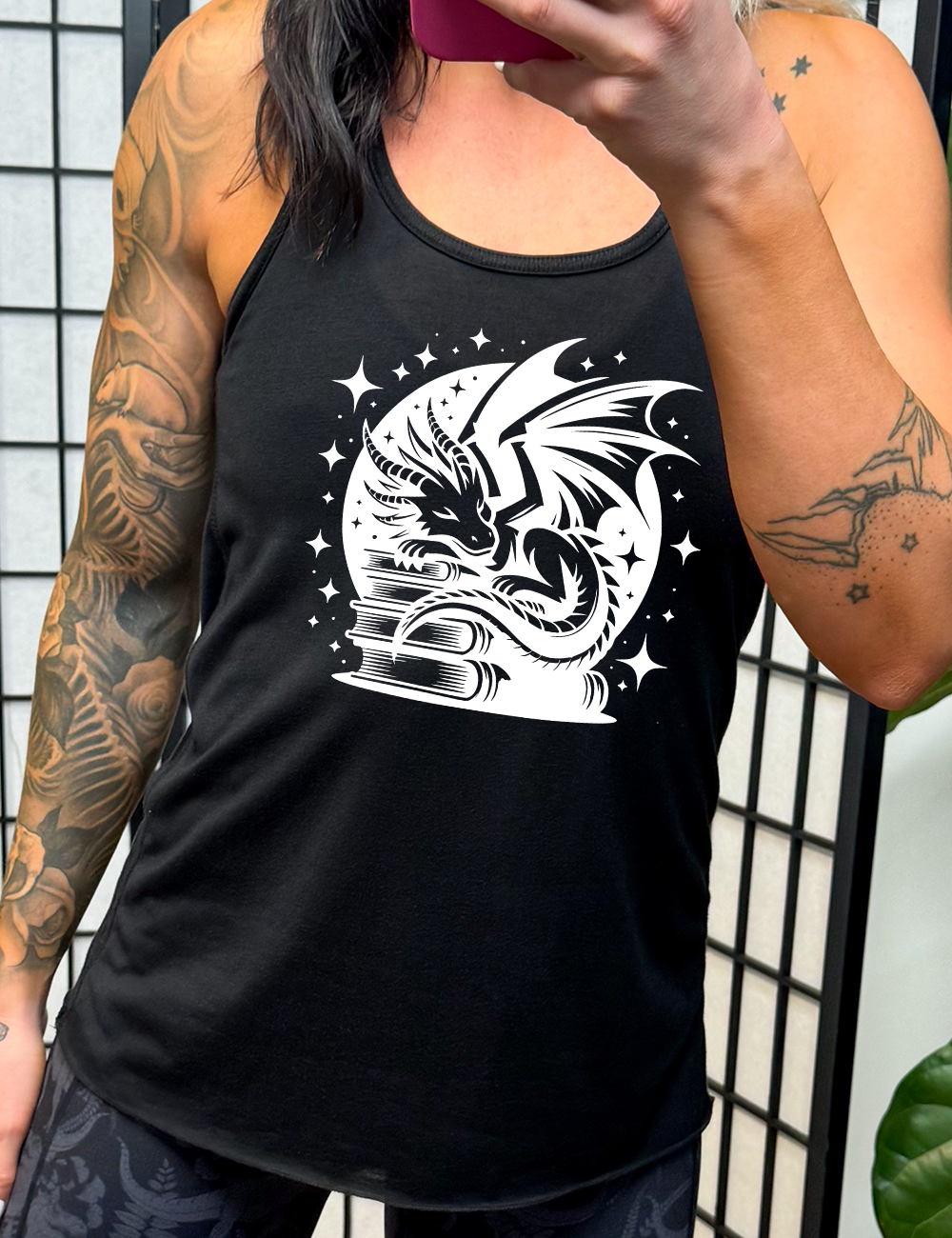 black racerback tank with the graphic of a dragon resting on a stack of books, in front of a full moon, with many stars around