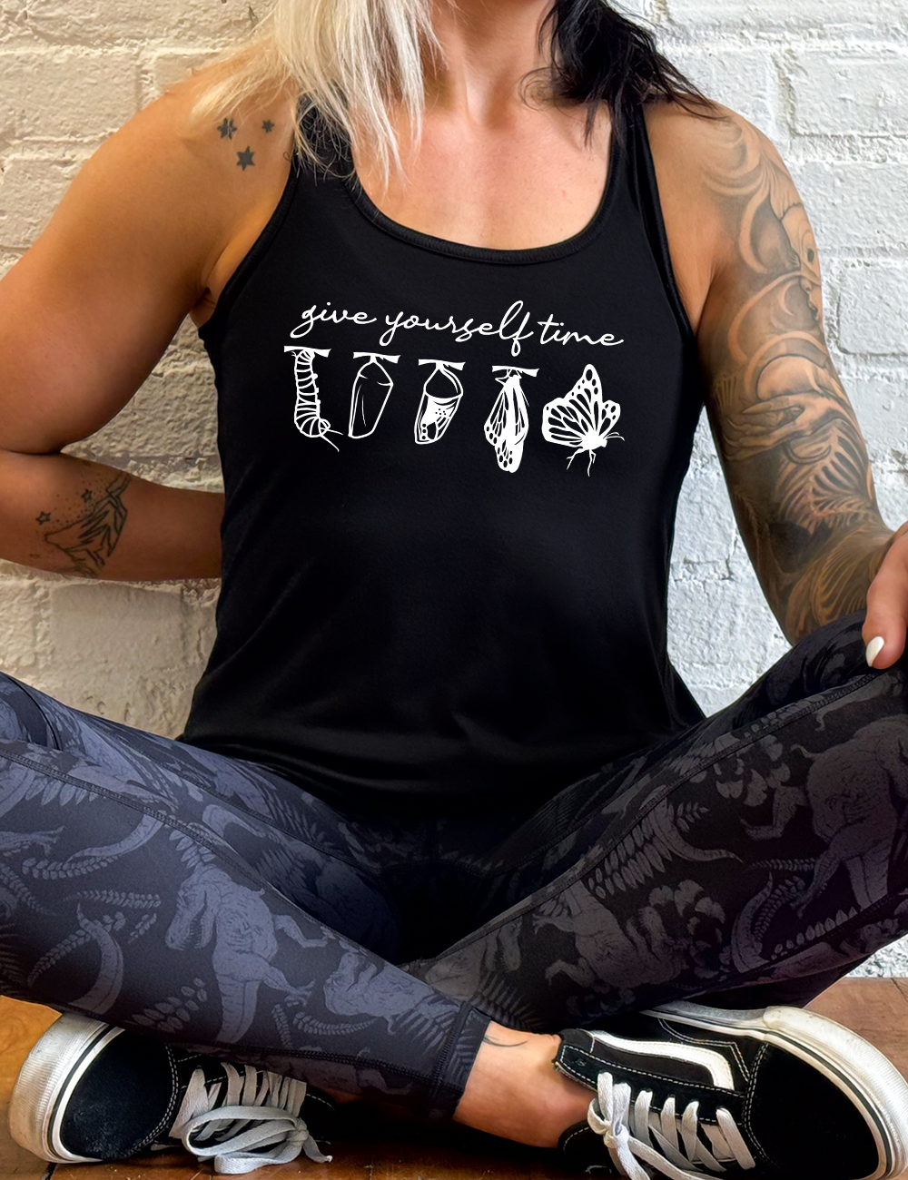 black flowy racerback tank with the graphic of the complete metamorphosis of a butterfly, with words above it saying "give yourself time"